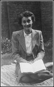 Woman kneeling on picnic blanket with open book in hands.