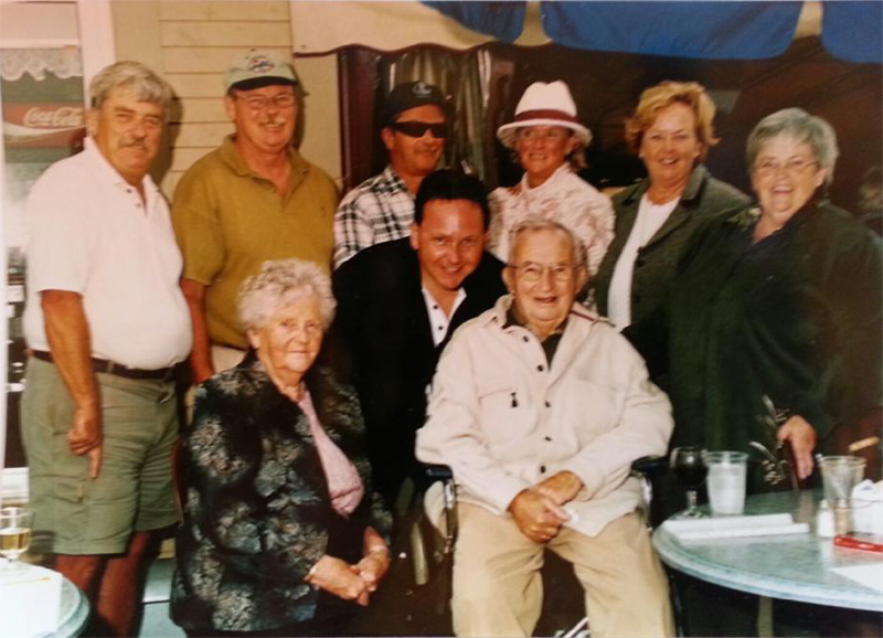 Group of family members are sitting and standing for a photo.