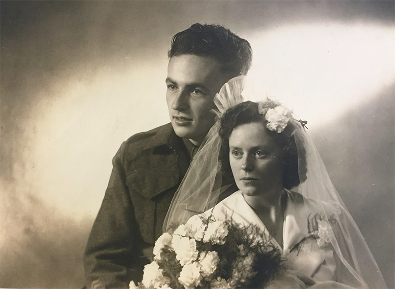A groom is wearing a uniform and the bride wears a wedding dress and holds flowers.
