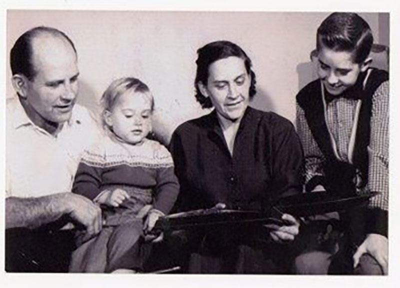 Man and woman look at an open book with their children.