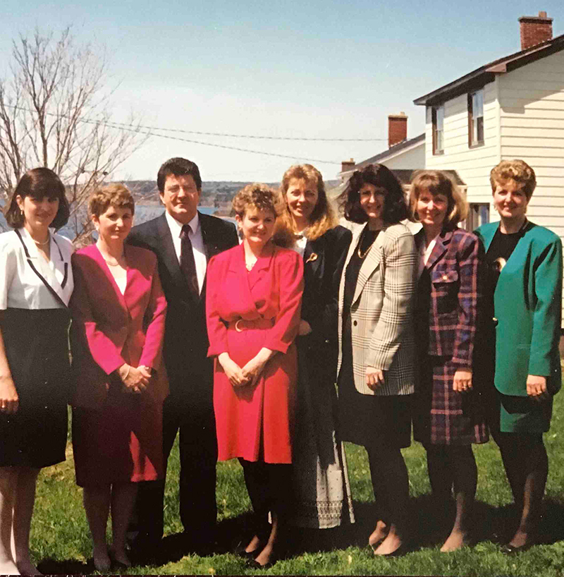 A family of seven adults stand on the front lawn of their house.