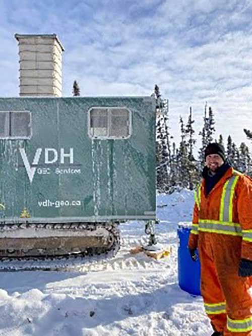 Young man in safety gear stands next to a large machine for travelling on snow.