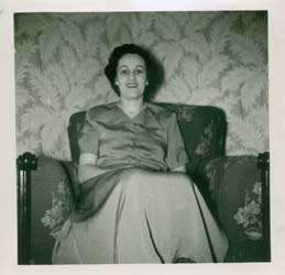 Joan in blouse and skirt, sitting on the sofa of a living room.
