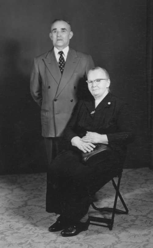 A woman in black sits next to a man who stands behind her.