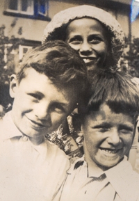 Close-up of two little boys in white shirts, and girl in hat behind them.