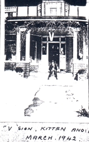 Very old photo showing young boy in front of a house.