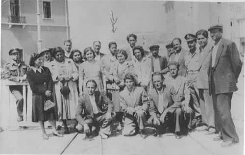 A large group of passengers stand on the pier waiting to board their ship.