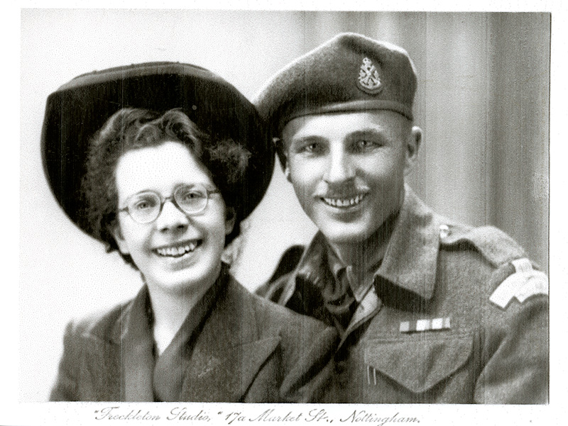 Well dressed beautiful lady and handsome man wearing military uniform sitting next to each other.