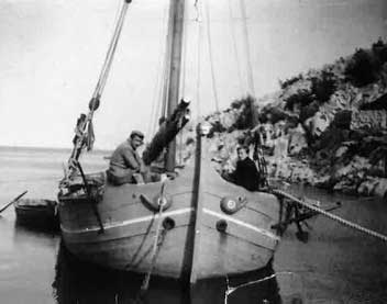 Black and white archival image of a ship, with two men sitting on the deck.