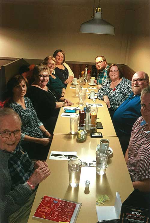 A family sits around two long tables in a restaurant, there is a red birthday card on the table.