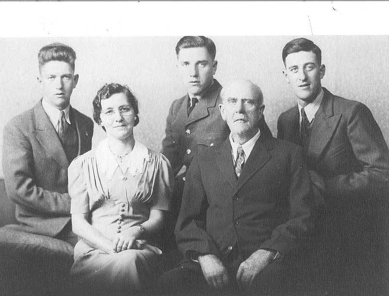 A man and woman sit for a portrait, there are three young men seated behind them.