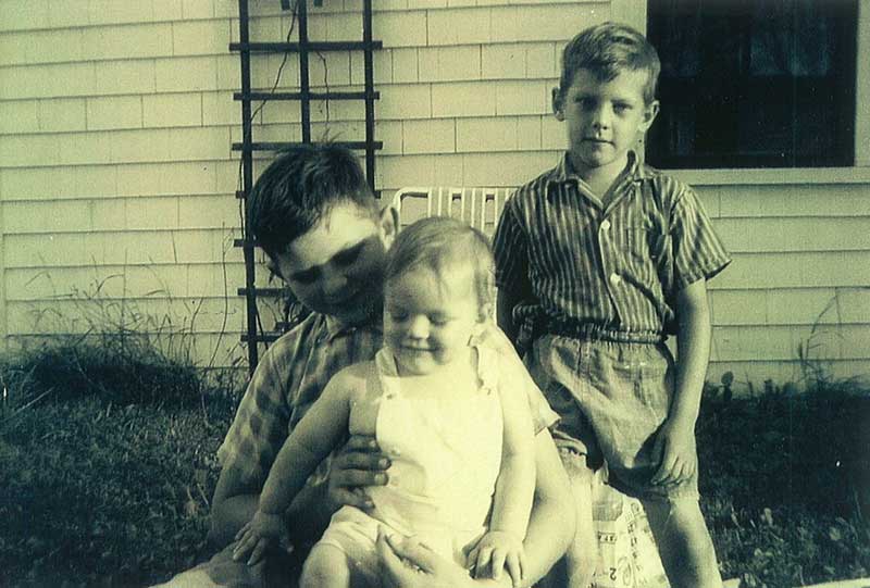 Three children sit on lawn chairs in front of a house.