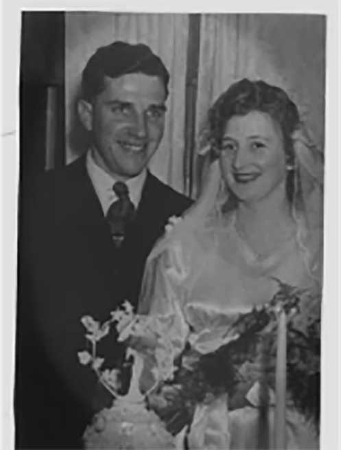 A bride and groom stand behind a cake on their wedding day.
