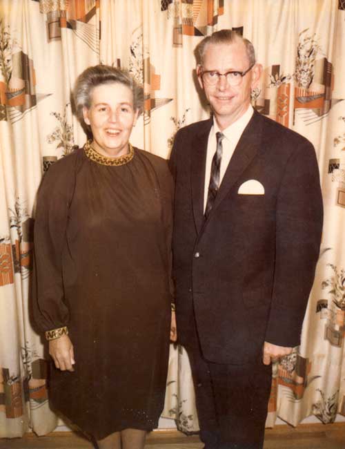 A well-dressed couple stand in front of a backdrop for photos.