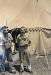 Young man in military uniform standing in front of transport truck.