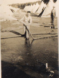 Young men using hose in a field with rows and rows of tents.
