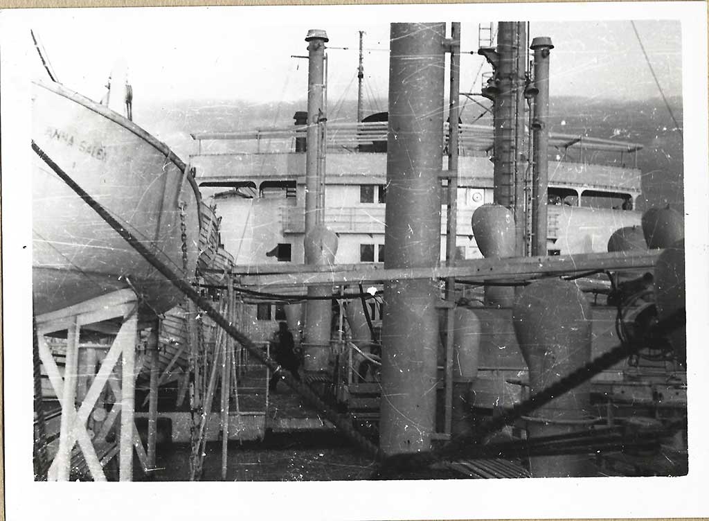 Black and white photo of a ship's deck with a lifeboat to the left.