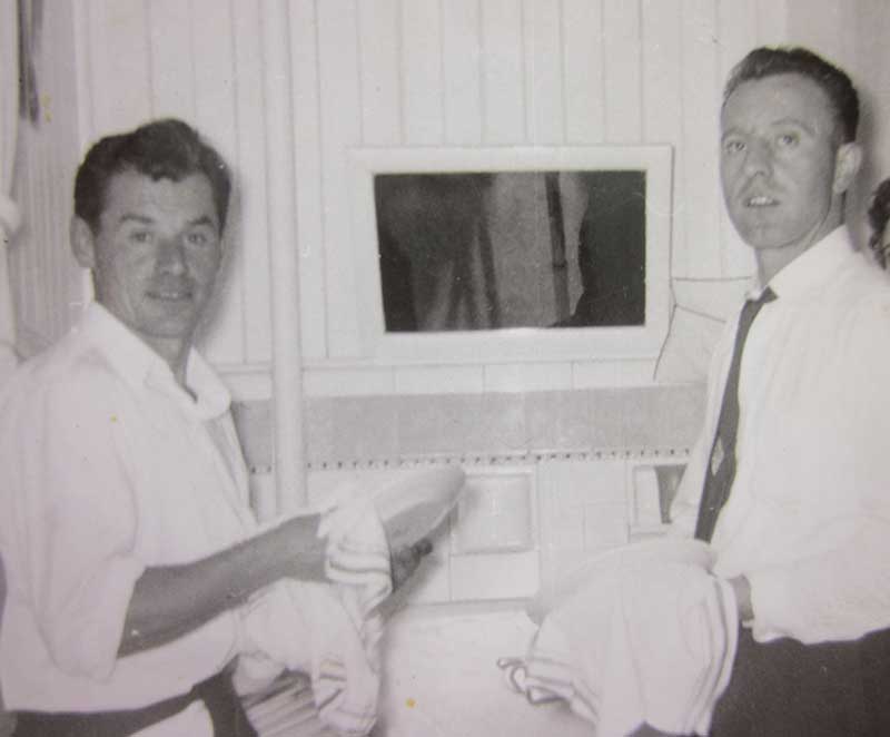 Two men stand on either side of a sink as they wash dishes.