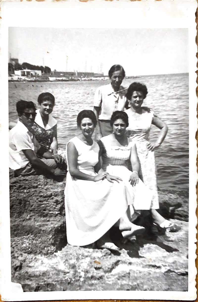 A group of people sit on large rocks near the ocean.