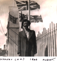 Young Norma, standing in front of buildings with British flags flying in background.