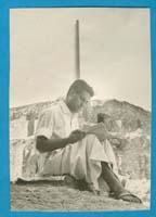 Young man in white robe, sitting and reading.