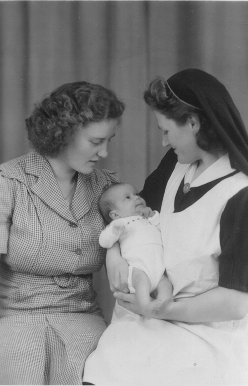 Two beautiful ladies are looking at a small baby.