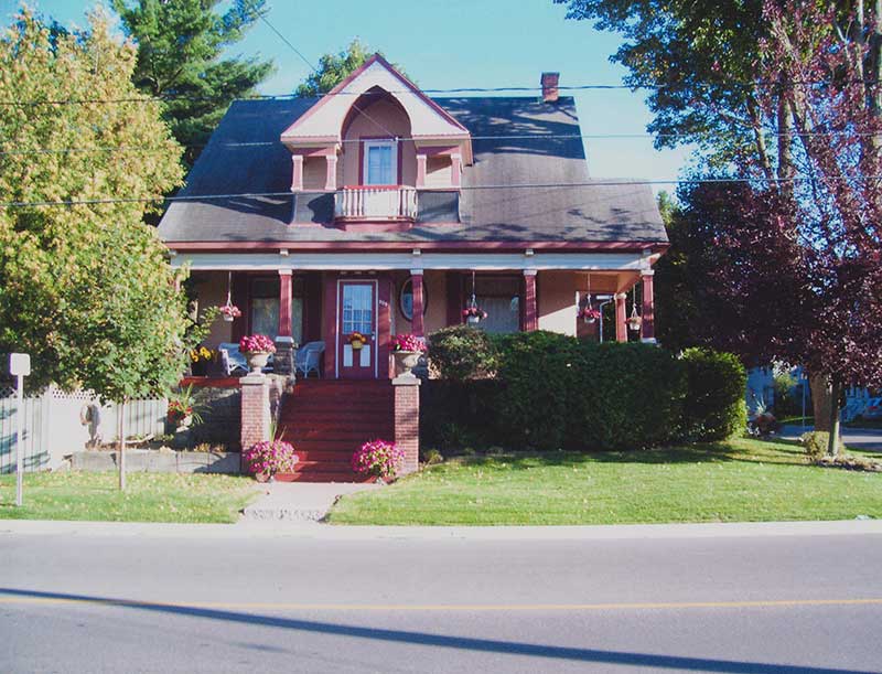 A nice coral-coloured house as seen from across the street. There are lots of flowers and a hedge surrounding the house.