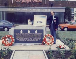 Art standing next to war memorial with two wreaths leaning against it.