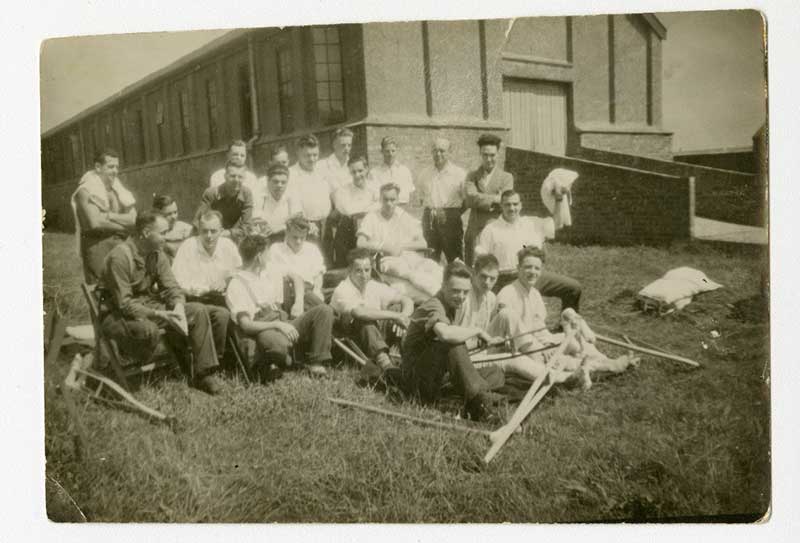 A large group of young men sit and stand around in a field.