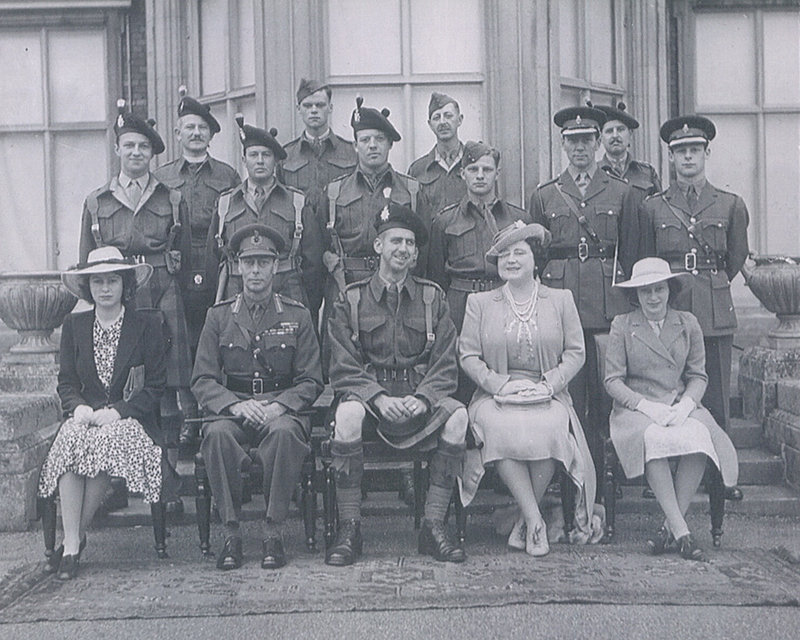 A group of men in military stand behind members of the Royal Family.