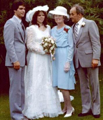 A scene from a wedding with the bride and groom standing on a green lawn and an older couple stand beside them.