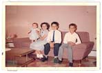 Small colour photograph of a mother sitting on a pink couch with three children.