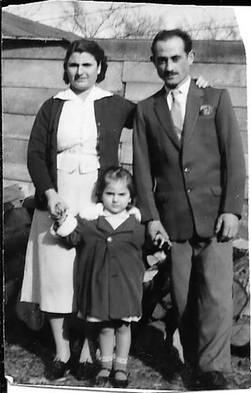 Man and woman stand with a child between them and each one holds her hand.