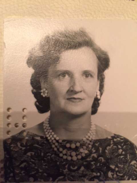A woman wearing pearls and earrings sits for a passport photo.