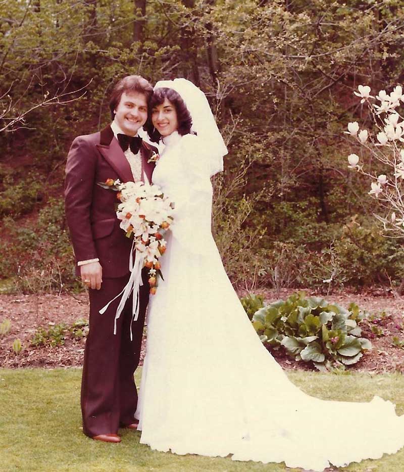 Young bride and groom are posing in front of garden and trees.