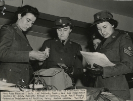 Three female officers looking in a sports bag and holding papers.