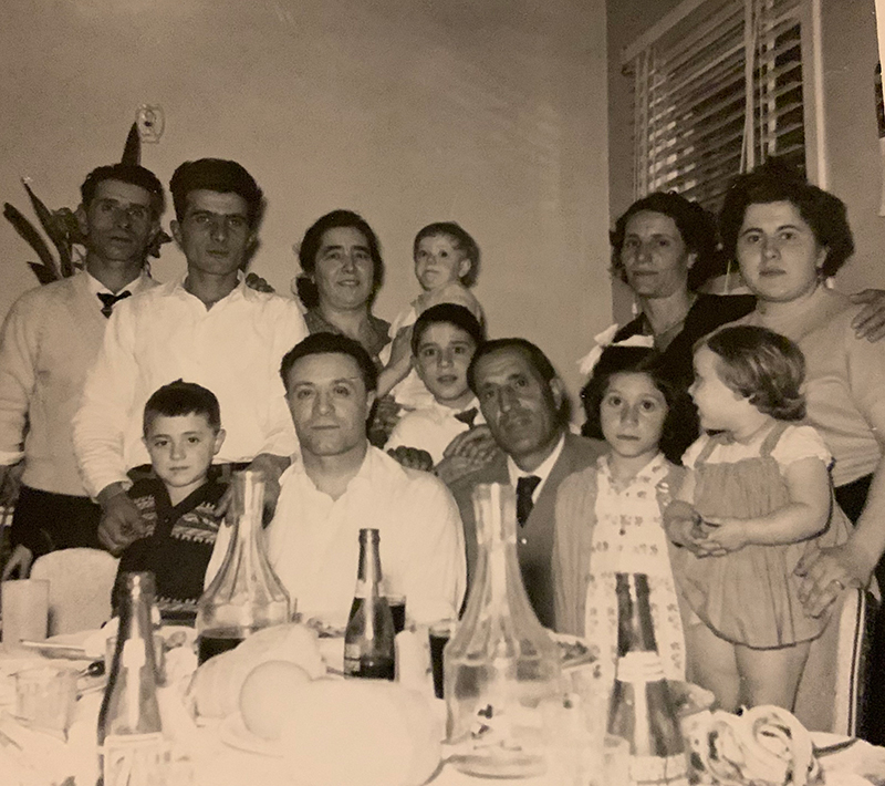 Large group of people behind a table laden with food and drink.