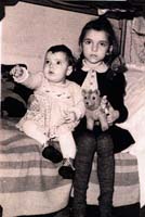 Little girl and a baby sitting on the edge of a bed.