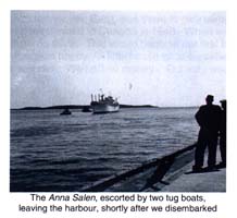 Two people standing on the dock, watching a ship sail in the harbour.