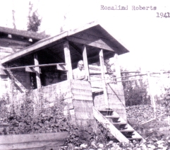 Old photograph of a woman looking outside from the porch of a house.