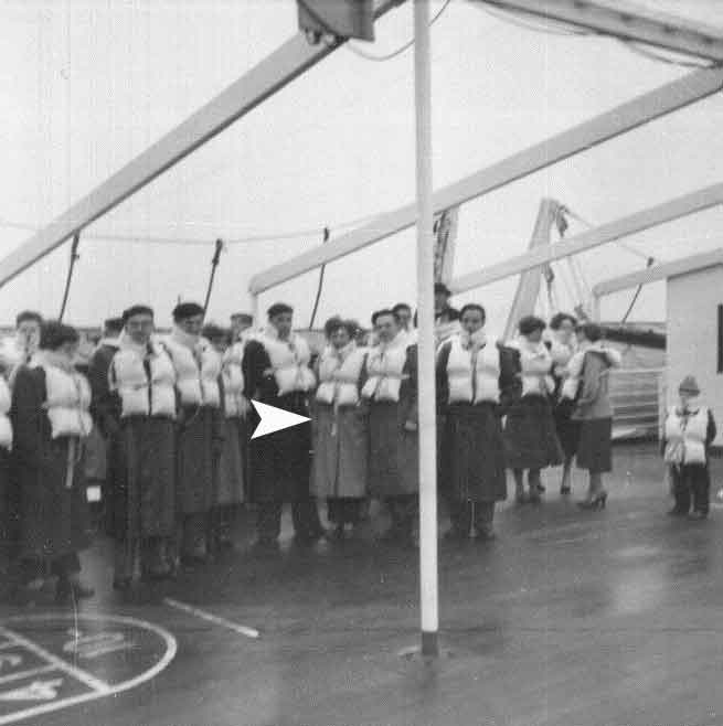 Group of man and women standing on ship wearing life jacket.