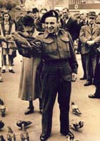 Young Henry in uniform throwing food to the pigeons at his feet.