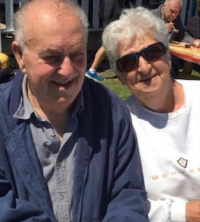 A man and a woman sitting outside smile at the camera.