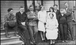 Group of people outside of house sitting and standing for photo.