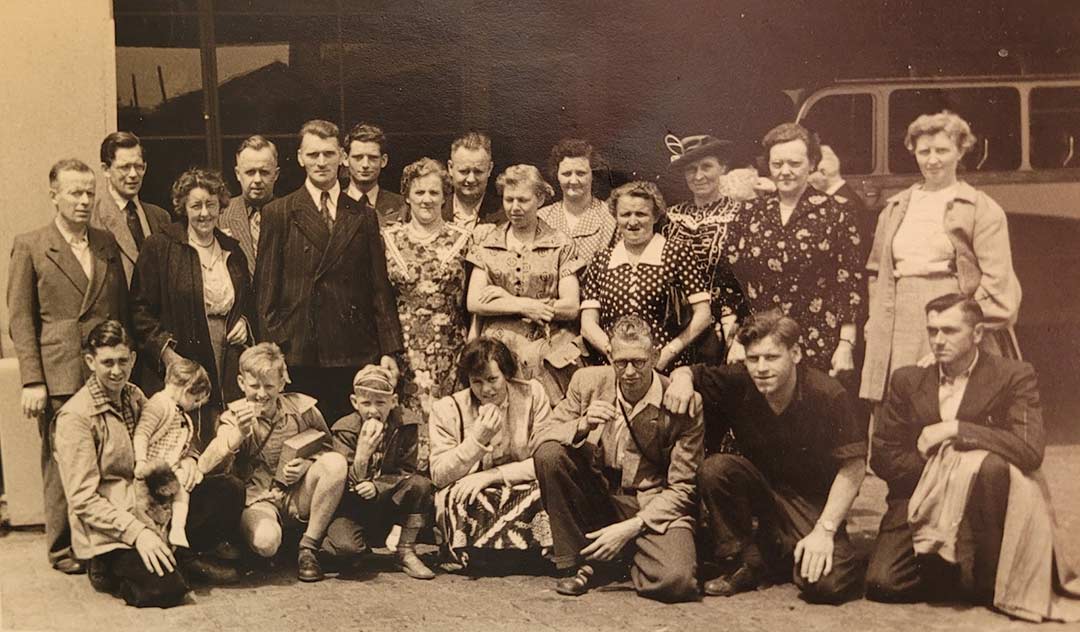 Sepia toned photo of a large group of Dutch people on a Rotterdam pier, Cornelia van Herk is kneeling in the front row with her siblings.