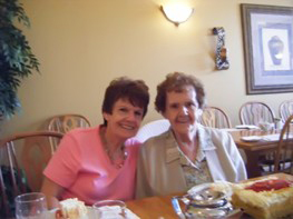Daughter Pauline is photographed alongside her mother Joan at the latter's birthday celebration, seated behind a table.