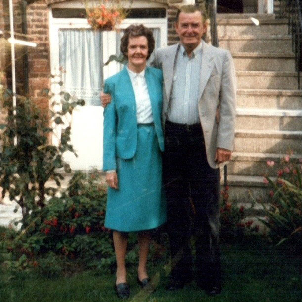 Joan and Les pose with his arm around her in the garden of Joan's old house in London.
